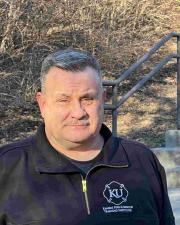 Photo of Ken Fowler in an blue KFRTI shirt standing in front of a wooded area